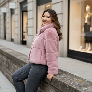 Woman in a pink coat sitting on a ledge in front of a store window
