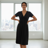 Woman wearing a black dress standing in a room with large windows.