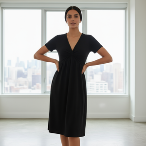 Woman wearing a black dress standing in a room with large windows.