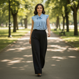 Woman walking in a park wearing a light blue blouse and black pants.