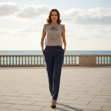Woman in a beige blouse and navy pants standing on a paved walkway with a scenic background.