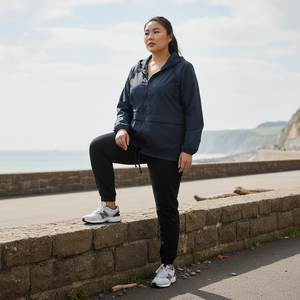 Woman in navy jacket and black pants sitting on a stone wall by a coastal path