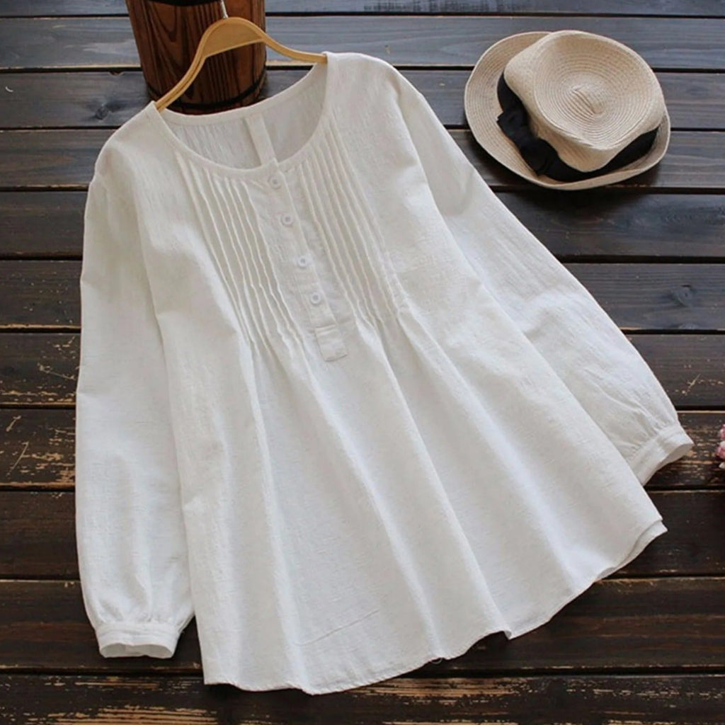 White blouse on a wooden surface with a hat in the background