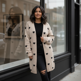 Woman wearing a long cream cardigan with black heart patterns standing in front of a store window.