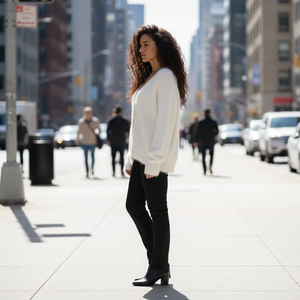Woman in a white sweater and black pants standing on a city street.