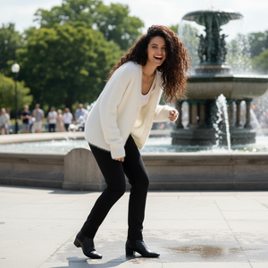 Woman in a white sweater and black pants laughing in front of a fountain
