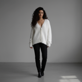 Woman wearing a white sweater and black pants against a gray background