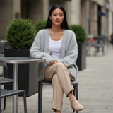 Woman sitting outdoors on a chair wearing a light gray cardigan and beige pants.