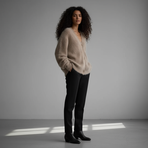 Woman wearing a beige sweater and black pants standing in a softly lit room.