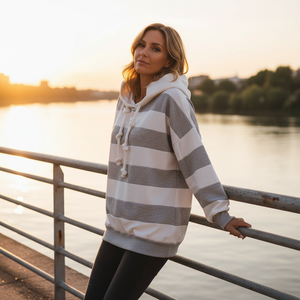 Woman wearing a striped hoodie by a waterfront at sunset