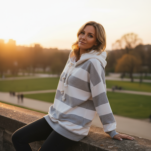 Woman wearing a striped hoodie sitting on a wall with a park background