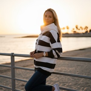 Woman wearing a black and white striped sweater by a body of water at sunset.