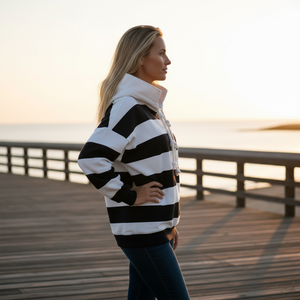 Woman wearing a black and white striped sweater on a wooden pier at sunset.