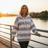 Woman wearing a striped hoodie by a body of water at sunset