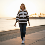 Woman walking on a path by a waterfront at sunset wearing a striped hoodie and jeans.