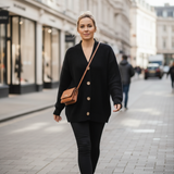 Woman walking on a city street wearing a black cardigan and carrying a brown bag.