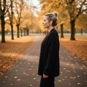 Woman in a black coat standing on a path lined with trees with autumn foliage.