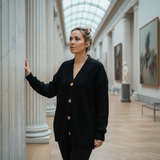 Woman in a black cardigan standing in an art gallery with columns and paintings.