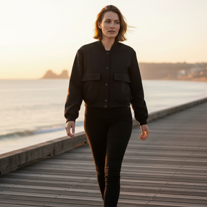 Woman walking on a wooden boardwalk by a body of water during sunset.