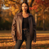 Woman wearing a brown leather jacket and black outfit standing in an autumn setting.