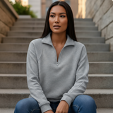 Woman wearing a gray zip-up sweater sitting on stone steps.