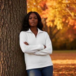 Woman in a white sweater standing against a tree with autumn foliage in the background