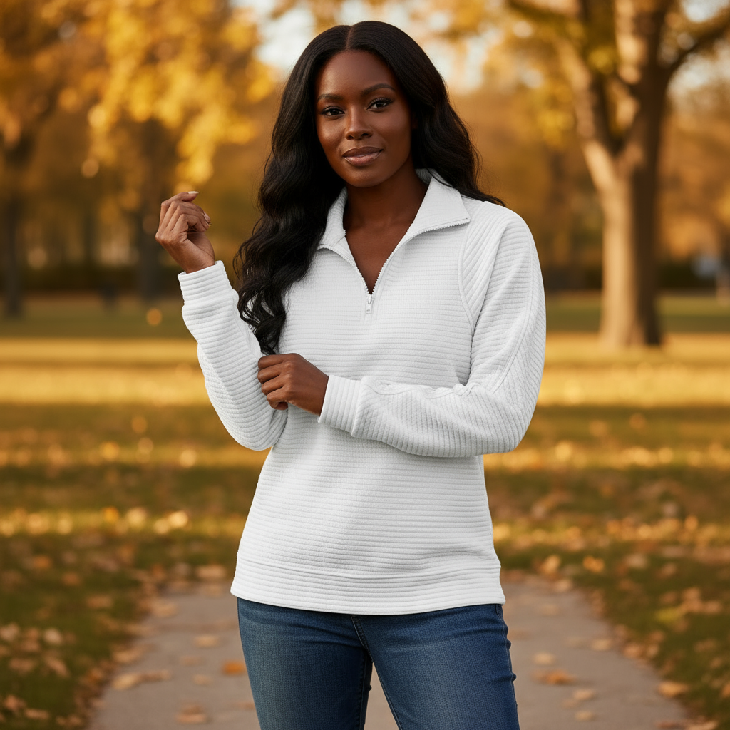 Woman wearing a white sweater and blue jeans standing in a park with autumn leaves.