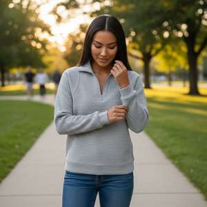 Woman wearing a gray sweater and blue jeans standing on a path in a park.
