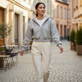Woman walking on a street wearing a gray hoodie and beige pants.