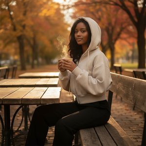 Woman in a white hoodie sitting on a bench in an autumn park, holding a steaming cup.