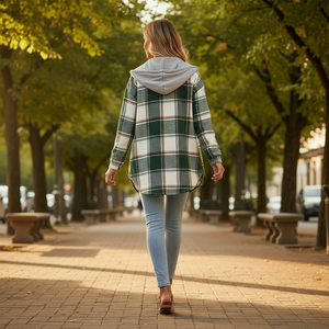 Woman walking on a tree-lined street wearing a plaid shirt and light blue jeans.