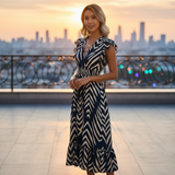 Woman in a black and white patterned dress standing on a rooftop with a cityscape in the background.