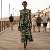 Woman in a green and white dress walking on a wooden boardwalk with people in the background.